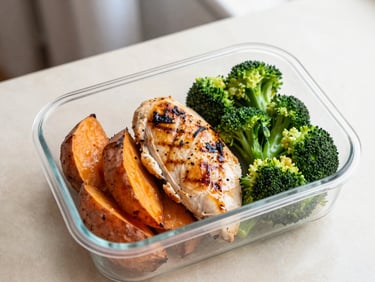 Overhead shot of grilled chicken breast with roasted sweet potatoes and steamed broccoli in a clean container, natural light