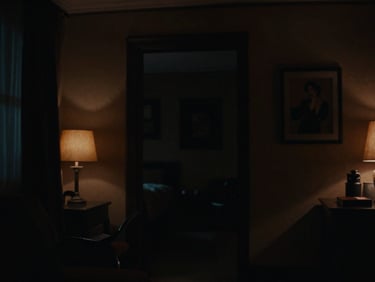 Cinematic anamorphic shot of a moody, low-key lit interior, deep shadows, rich color grading, subtle amber light source.