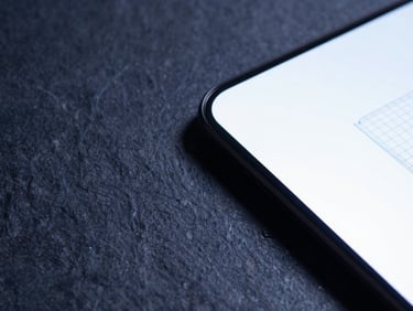 Macro flat-lay of dark slate stone texture next to a glowing ultra-thin OLED screen displaying a clean wireframe layout, sharp shadows, cool blue ambient light.
