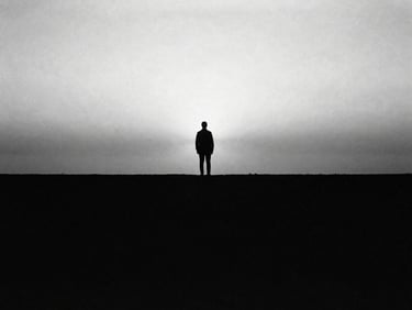 High-contrast black and white 35mm photo of a solitary figure in silhouette standing at the edge of a vast, misty horizon, dramatic chiaroscuro.