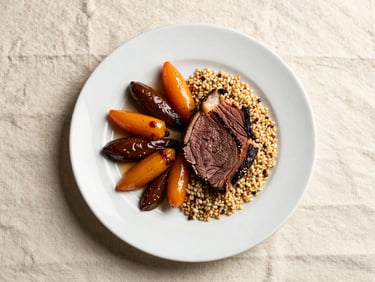 Overhead plating study of a full dinner plate—carved roasted beef, glazed root vegetables, and grain pilaf under professional north light on a cream linen surface