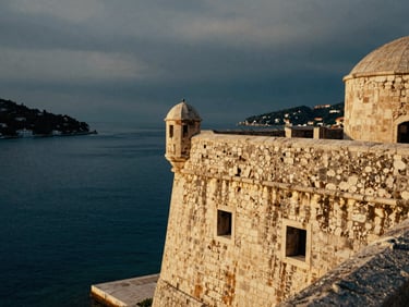Close-up of a weathered stone fortress overlooking a misty, deep blue harbor in Croatia, dramatic overcast daylight, cinematic 35mm composition.
