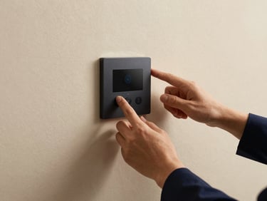 Hands adjusting a sleek climate control panel mounted on a textured plaster wall, soft warm side-lighting.
