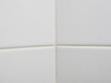 Close-up macro shot of perfectly aligned large format white tiles with minimal grout lines in a modern bathroom, showcasing impeccable mitered edges where two surfaces meet. Sharp focus on texture and precision.