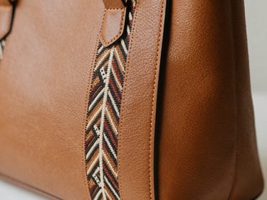 Macro details of a structured leather bag featuring a perfectly integrated geometric tenun textile accent, warm studio light