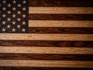 High-contrast close-up of a laser-engraved wooden American flag, showing detailed grain of Baltic birch and precise dark etched stripes under warm workshop light