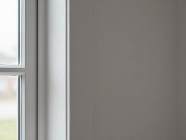 Tight close-up of a freshly painted interior wall edge meeting white trim, bright even daylight from a window off-frame left, paint line razor-straight with no bleed, roller marks smoothed flat, no people visible