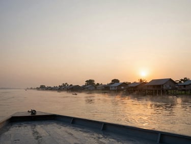 Sunrise from the upper deck of a river vessel on the Mekong, low mist over the water, wooden stilted villages on the far bank emerging from the haze, warm amber horizon light, wide panoramic framing with generous sky