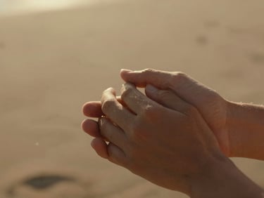 Close-up of hands gently holding each other, warm golden-hour sunlight streaming from behind, soft dust particles in the air, cinematic 35mm film look