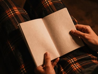 A warm-toned close-up of textured heavy flannel fabric and hands holding an old independent zine, low-key lighting, copper and charcoal color palette, atmospheric film texture