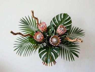 Flat-lay overhead of a seasonal floral arrangement with tropical foliage, proteas and sculptural stems on a cool white background, even studio lighting, minimal and precise