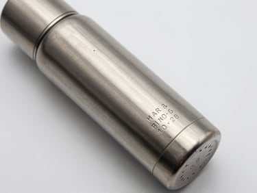 Close-up overhead flat-lay of a stainless steel thermal flask on a white surface, laser-engraved name and date visible in crisp relief on the metal body, studio north-light, no shadows, clean neutral background
