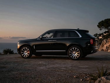 Cinematic profile of a black late-model luxury SUV parked on a quiet Ibiza cliffside at dusk, deep shadows, subtle gold reflections.