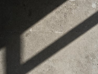 Macro detail of weathered concrete texture, hard natural sunlight casting deep geometric shadows across the surface.