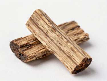 Close macro study of agarwood chips on a plain white surface under neutral studio strobe, visible dark resin veins running through pale heartwood grain, documentary framing, no props