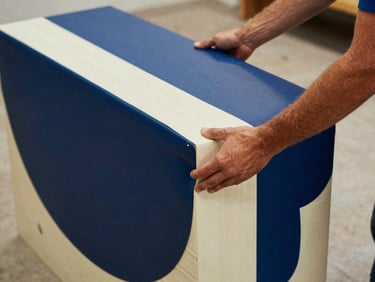 Close-up of a mover's hands securing tailored protective wrapping around a large, oddly shaped art piece, warm editorial photography, natural daylight.