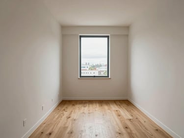 Entry-point view of a compact studio apartment, even overcast daylight through a single window, pale walls, clean laminate flooring, no furniture, architectural detail
