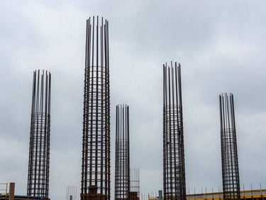 Vertical steel reinforcement cages for columns standing tall against an overcast sky on an active industrial construction site.