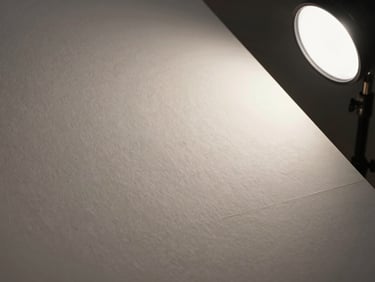 Close-up of laminated paper sheet surface under angled north-facing daylight, showing smooth seal coating and print registration edge, defect-free finish, studio strobe on right side