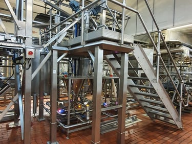 Industrial stainless steel processing machinery with metal stairs on a red brick factory floor.