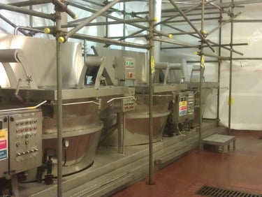 Industrial stainless steel boiling kettles in a food processing facility with safety scaffolding.