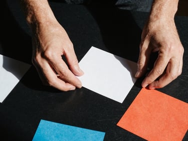 Extreme close-up of hands arranging raw creative mockups on a black studio table, sharp flash lighting, high-contrast shadows, 35mm film.