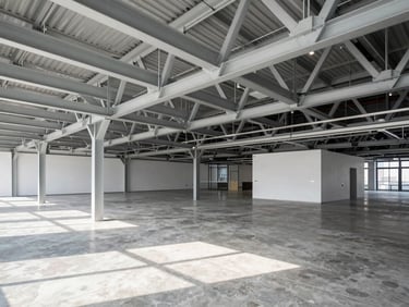 Wide shot of a modern commercial office interior with exposed steel trusses and clean concrete floors, natural daylight