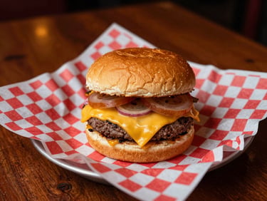 A golden-brown double cheeseburger with melting American cheese on a toasted bun, served on classic red-and-white checkered paper liner, warm tavern lighting.