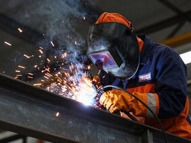 Close-up of a certified welder in full protective PPE welding a heavy steel structural beam, bright orange sparks, dark metallic background.