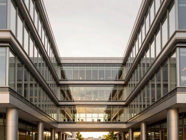 Symmetrical architectural shot of a modern commercial office lobby, steel and structural glass elements, clean lines, soft overcast daylight.