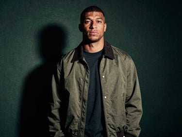 Low-key dramatic portrait of a modern footballer in high-fashion streetwear, cinematic shadows, desaturated tones, 35mm grain.