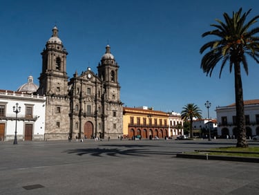 Wide environmental shot of Plaza de Armas in Santiago centro at midday, colonial cathedral facade on the left third, open plaza geometry and palm trees under deep blue sky, minimal foot traffic