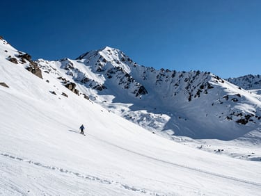 Wide shot of Valle Nevado ski terrain at high altitude, bright midday sun on white snow, sharp rocky Andean peaks in the background, a lone ski run cutting through the left third, deep blue sky