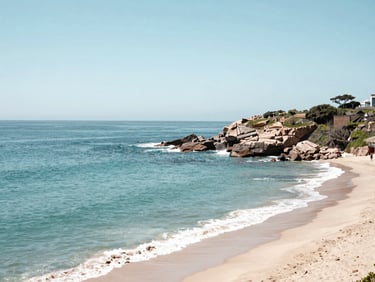 Wide coastal panorama of Viña del Mar at midday, turquoise Pacific water meeting a pale sand beach, rocky headland in the right third, bright sky above, no people