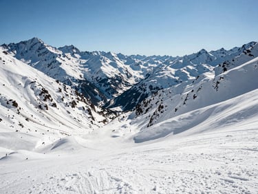 Wide valley view at Valle Nevado ski resort at midday, snow-covered slopes in the foreground, Andean peaks rising steeply behind, bright high-altitude daylight, no skiers in foreground, scale of mountain range dominant