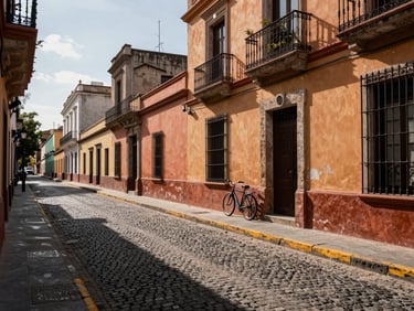 Wide landscape view along a historic street in Barrio Lastarria Santiago, colonial-era building facades in ochre and terracotta lining a narrow cobblestone lane, afternoon sun casting long geometric shadows across the pavement, a single bicycle leaning against a wall in the mid-ground