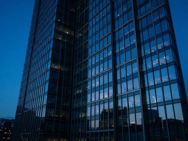 Sleek corporate photography of modern high-rise office windows reflecting a deep blue twilight sky, architectural lines, cool tones.