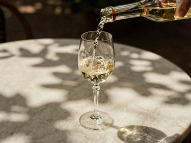A crisp pour of white wine into a delicate crystal glass on an outdoor marble table, dappled sunlight filtering through leaves