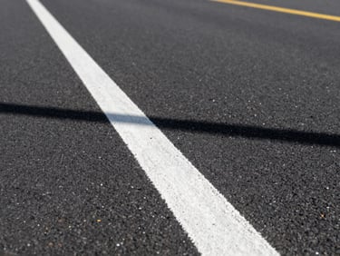 Low-angle 35mm perspective shot following a freshly painted crisp white line on dark asphalt, crisp morning sun casting sharp shadows, industrial utility
