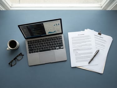 Top-down flat lay of neatly organized legal documents, a modern laptop, and a sleek pen on a slate blue office desk, bright natural daylight, professional editorial photography