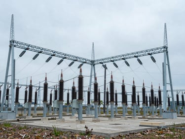 Wide environmental shot of a modern electrical substation integrated into a cool overcast landscape, desaturated steel-blue tones, 35mm