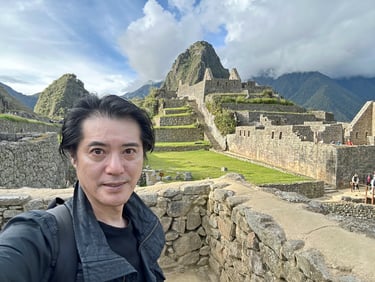 ペルーの世界遺産マチュピチュ遺跡を背景に立つ笹野大輔編集長。石造りの遺構と山々が広がる高地の風景