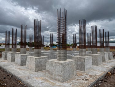 Extreme wide shot of a massive concrete substation foundation with heavy steel reinforcement cages under dark overcast skies.