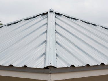 Close-up of metal roofing sheet seam and ridge cap on a completed Cameroonian residential building, overcast daylight, precise overlap and fastener pattern visible