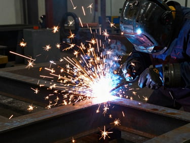 Active welding sparks flying in a dark workshop, bright arc-welding flares illuminating raw steel beams and heavy machinery