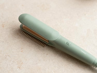 Overhead flatlay of a sage green Tymo hair straightener comb on a light stone surface, soft morning light