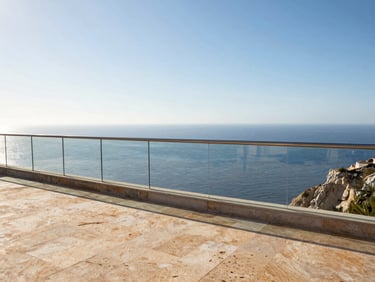 Panoramic establishing shot of a clifftop mirador on the Costa del Sol, long frameless glass railing spanning the viewing platform, bright sky and deep Mediterranean blue below, warm stone paving in foreground, no people