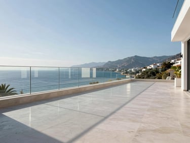 Wide-angle view of a contemporary Costa del Sol terrace, frameless glass balustrade running the full perimeter, white stone floor reflecting midday sun, sea and mountains visible beyond the transparent barrier, no people