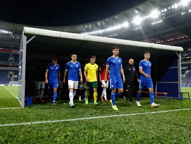 A football stadium tunnel with players walking out onto the bright green pitch, dramatic low angle