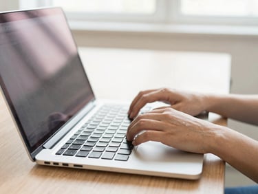 Hands typing on a modern laptop keyboard, clean computer lab environment, bright daylight